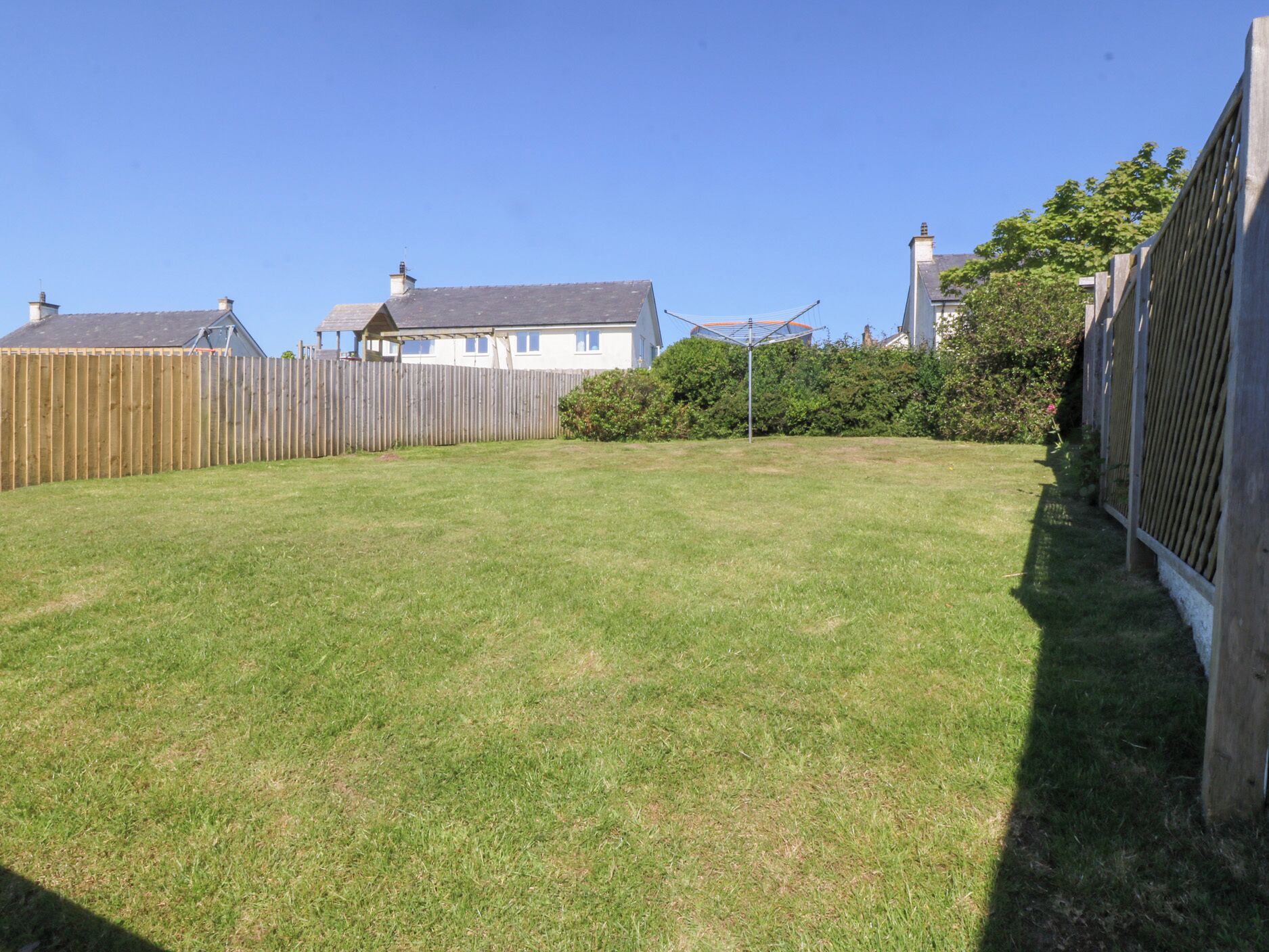 A grassy backyard with a wooden fence, a metal structure, and a house in the background.