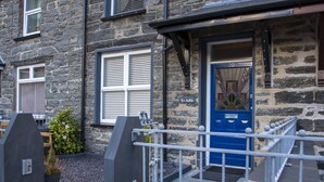 A stone building with a blue door, a small porch, and a metal railing. - Yr Adfa (Blaenau Ffestiniog)