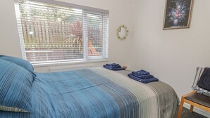 Ein Schlafzimmer mit Bett, Fenster mit Jalousien, einem Sessel und einem gerahmten Bild an der Wand.