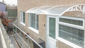 Ein Wohngebäude mit überdachter Terrasse, kleinem Garten und Holzzaun.