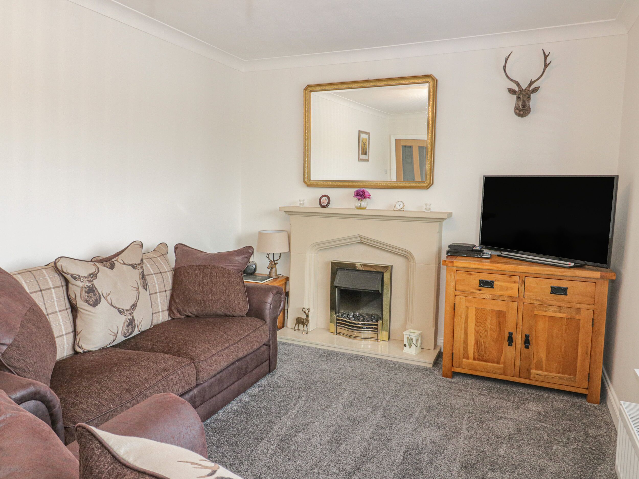 A living room with a brown sofa, a flat-screen TV, a wooden cabinet, and a fireplace.