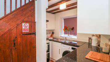 A kitchen with a wooden staircase, a washing machine, and a window with a vase of flowers.