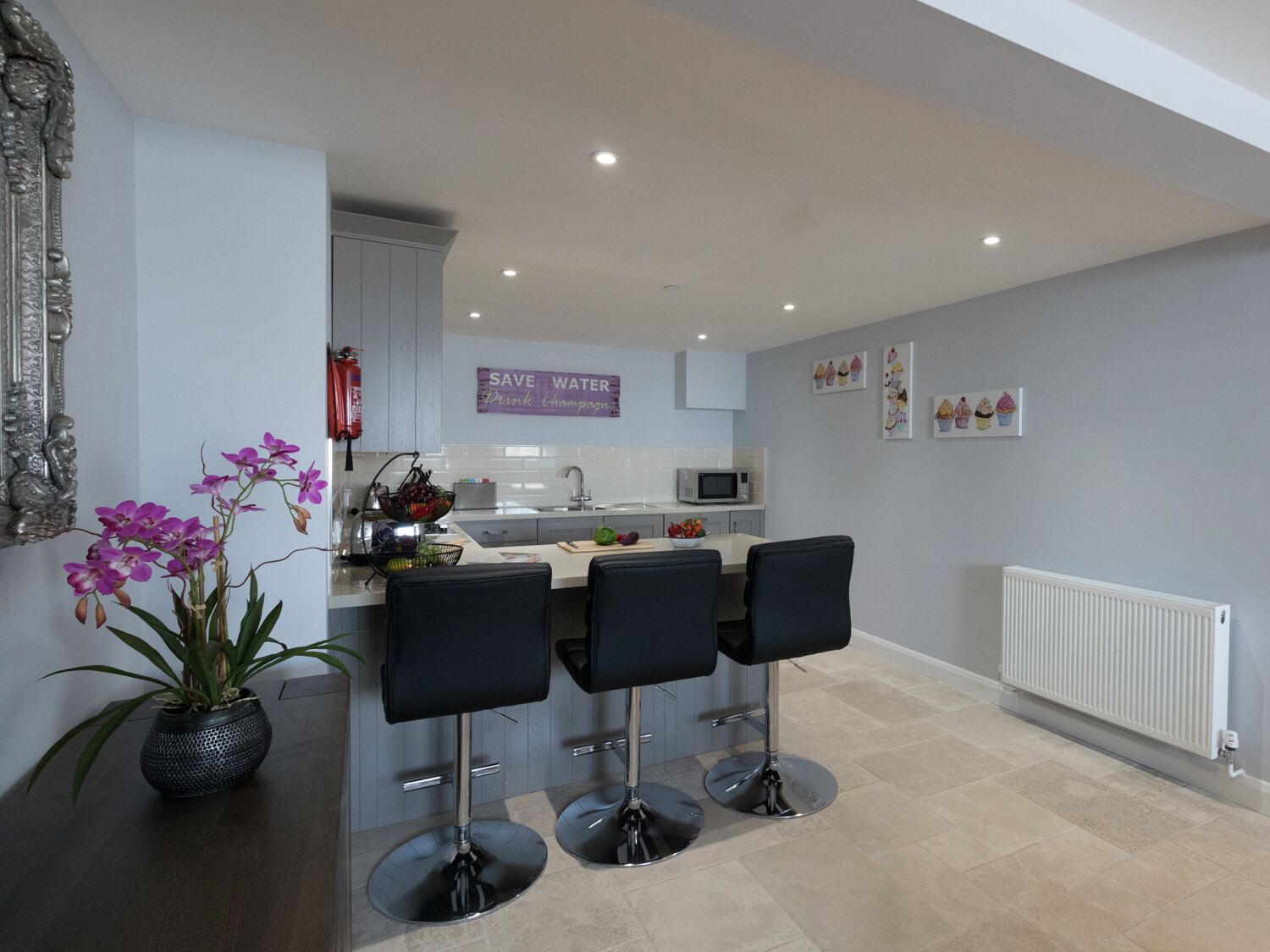 A modern kitchen with a central island, bar stools, and a potted orchid.