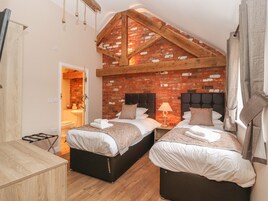 A bedroom with two beds, a brick wall, wooden beams, and a wooden floor.