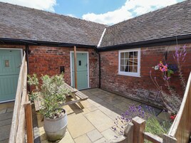A courtyard with a brick building, a green door, a window with a white frame, and a potted plant.