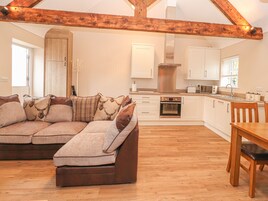 A cozy living area with a sofa, wooden beams, a kitchen with white cabinets, and a dining table.