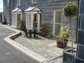 A stone building with a gravel patio, a table with chairs, and potted plants. - Bwthyn Llechen (Porthmadog)
