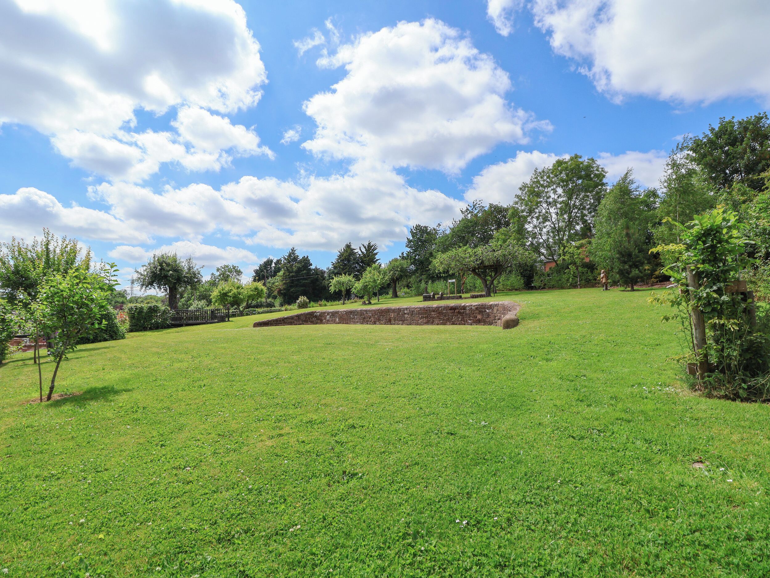 A grassy outdoor area with a stone wall and trees.