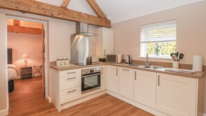 A modern kitchen with wooden beams, a built-in oven, a microwave, and a window with a view of trees.
