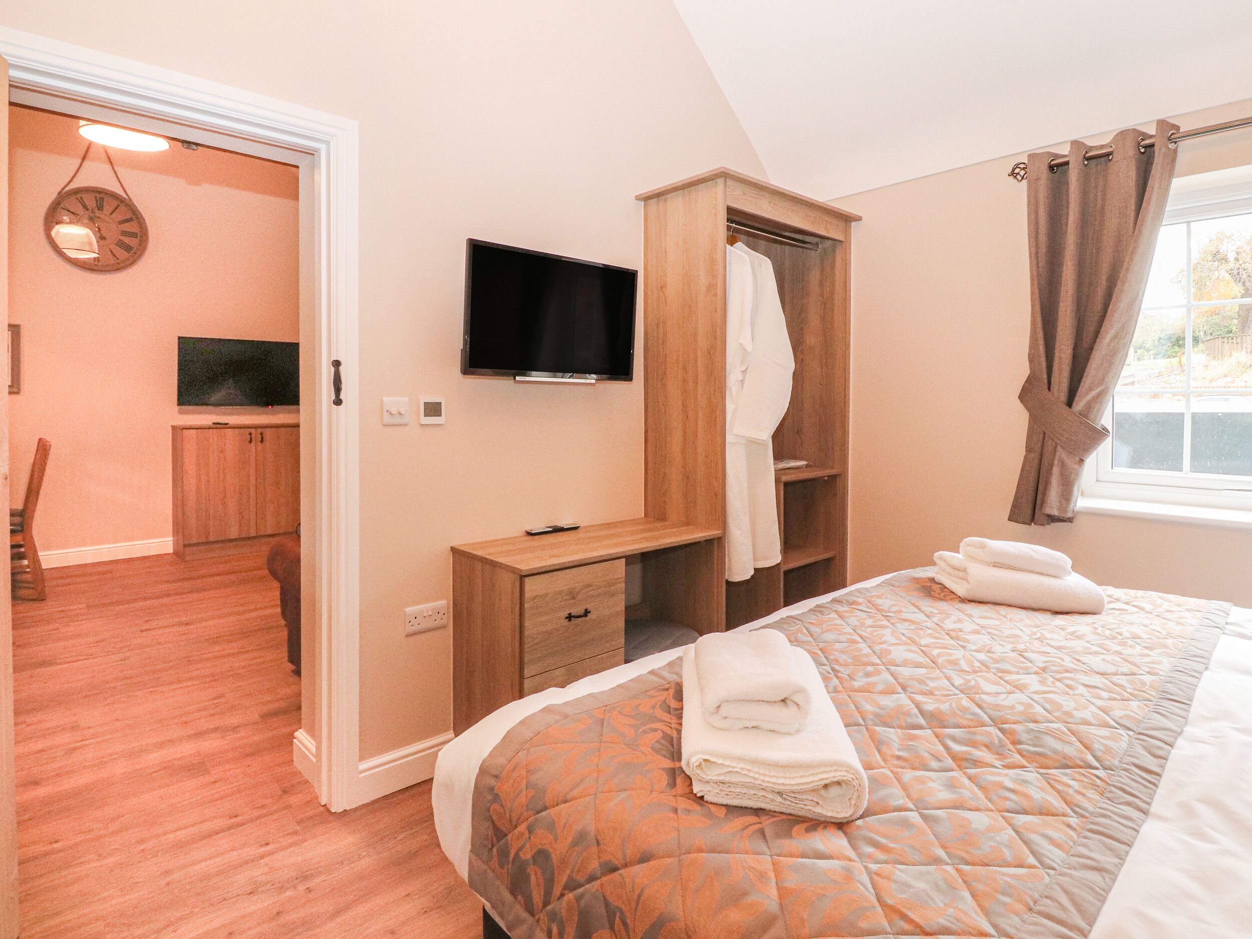 Ein Schlafzimmer mit einem Bett, einem Fernseher, einem Holzschrank und einem durch eine offene Tür einsehbaren Badezimmer.