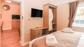 Ein Schlafzimmer mit einem Bett, einem Fernseher, einem Holzschrank und einem durch eine offene Tür einsehbaren Badezimmer.