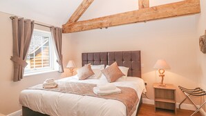 A neatly made bed with a headboard, two bedside lamps, and a window with curtains.