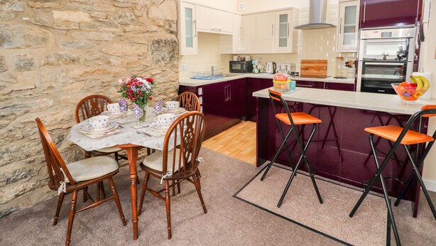 A compact kitchen with a stone wall, wooden dining table, and bar stools.