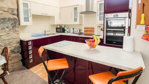 A compact kitchen with a stone accent wall, a central island with stools, and a refrigerator with a hanging vegetable.
