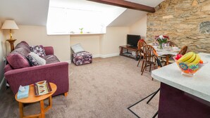 A cozy living room with a purple sofa, a small round table, a TV, and a dining area with chairs and a table set for two.