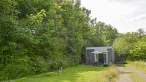 A rustic stone building with a door open, a picnic table, and a path leading to it. - Engine House (Exeter)