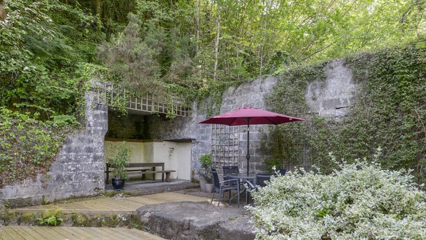 A rustic outdoor seating area with a wooden deck, stone walls, and a red umbrella. - Engine House (Exeter)