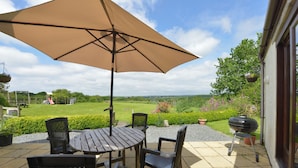 An outdoor patio with a table and chairs, a large umbrella, and a barbecue grill. - Valley View (Helston)