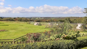 A rural landscape with a grassy field, a wooden fence, and a small structure in the distance. - Valley View (Helston)