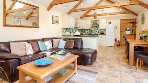 A spacious living room with a leather sofa, a wooden coffee table, and a kitchen in the background. - Valley View (Helston)