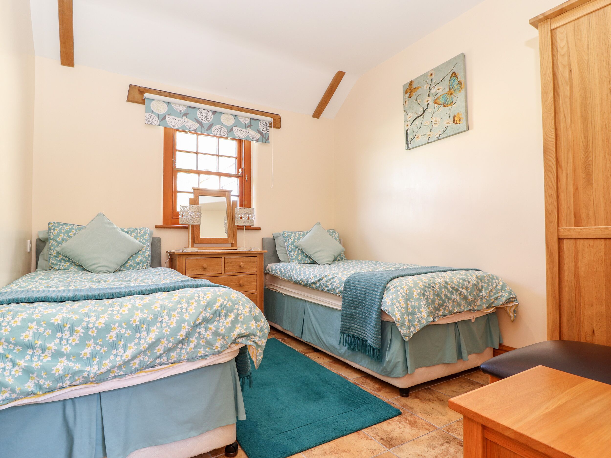 A bedroom with two beds, a dresser, a window with a floral curtain, and a wooden wardrobe.