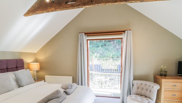 Une chambre à coucher avec un grand lit, une chaise, une commode et une fenêtre avec des rideaux.