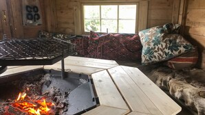 Un interior de cabaña acogedor con un estufa de leña, una ventana con vistas a la vegetación y una manta estampada sobre un sofá.