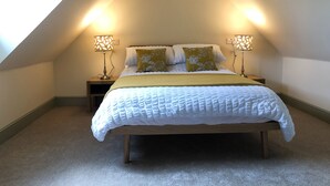 Un dormitorio con techo inclinado, una cama con ropa de cama blanca, dos lámparas de noche y una manta verde.