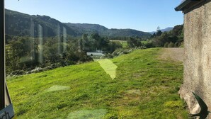 Vista de un campo cubierto de hierba con un edificio de piedra y una montaña al fondo.