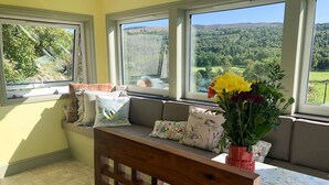 Una habitación con un ventanal grande, un banco de madera y una mesa con mantel floral.