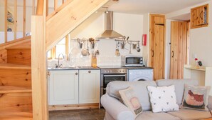 A cozy kitchen with a wooden staircase, white cabinets, and a grey sofa with decorative pillows. - High Grove (Ludlow)