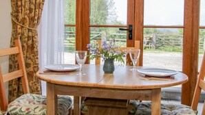 A wooden table set for two with a vase of purple flowers, two wine glasses, and plates. - High Grove (Ludlow)