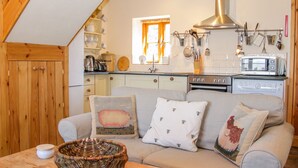 A cozy kitchen with a wooden ceiling, a built-in oven, and a microwave. There is a window with curtains, and various kitchen utensils are visible. - High Grove (Ludlow)