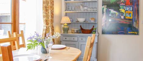 A dining area with a wooden table, chairs, a vase with flowers, and a painting on the wall.