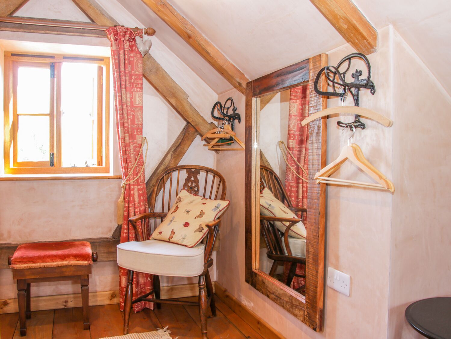 Ein gemütliches Zimmer mit einer Holzbank, einem Sessel mit Kissen, einem Spiegel und einem Fenster mit Vorhängen.