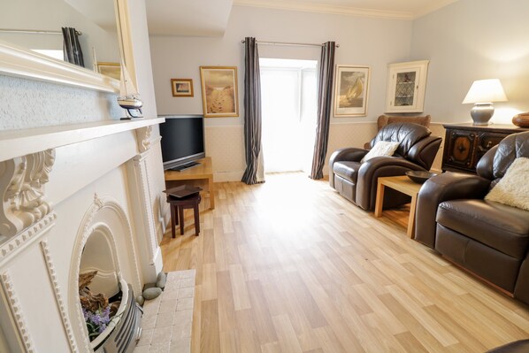 A living room with a fireplace, a leather sofa, a television, and a wooden floor.