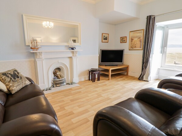 A living room with a fireplace, a television on a wooden stand, and a large mirror above it. - Abermaw Views (Barmouth)