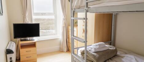 A bunk bed room with a TV, a heater, and a window with curtains.
