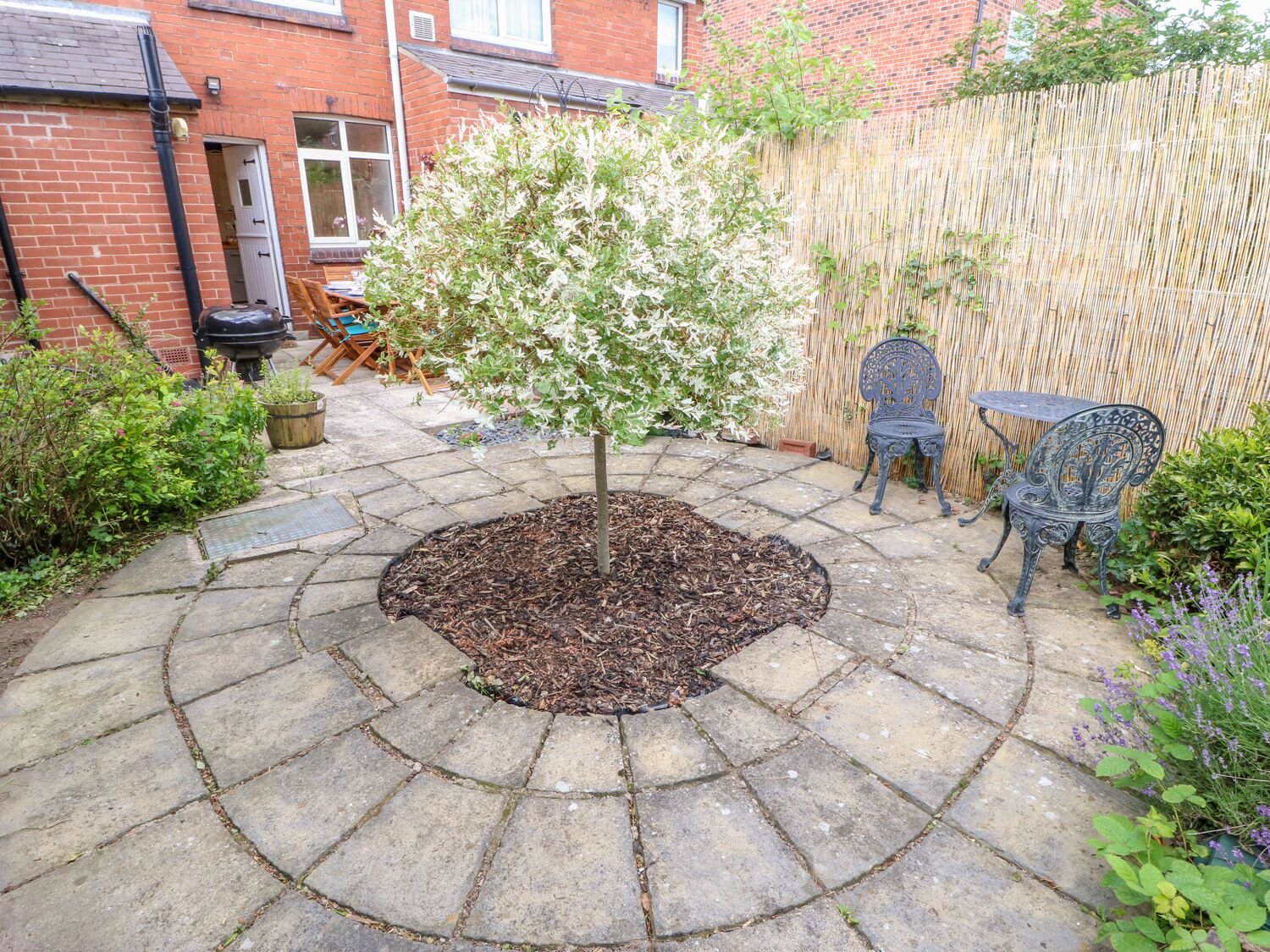 A patio with stone paving, a small tree, a bamboo fence, and outdoor furniture.