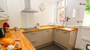 A compact kitchen with a wooden countertop, a built-in stove, and a window with a view of greenery. - Mallard Cottage (Tadcaster)