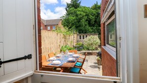 An open patio with a wooden table set for dining, surrounded by a bamboo fence and a small tree. - Mallard Cottage (Tadcaster)