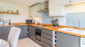 A modern kitchen with grey cabinets, a wooden countertop, a built-in oven, a microwave, a toaster, and a sink with a faucet. - Grooms Cottage (Leicester)