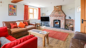 A cozy living room with a fireplace, a sofa, a coffee table, and a television. - Grooms Cottage (Leicester)
