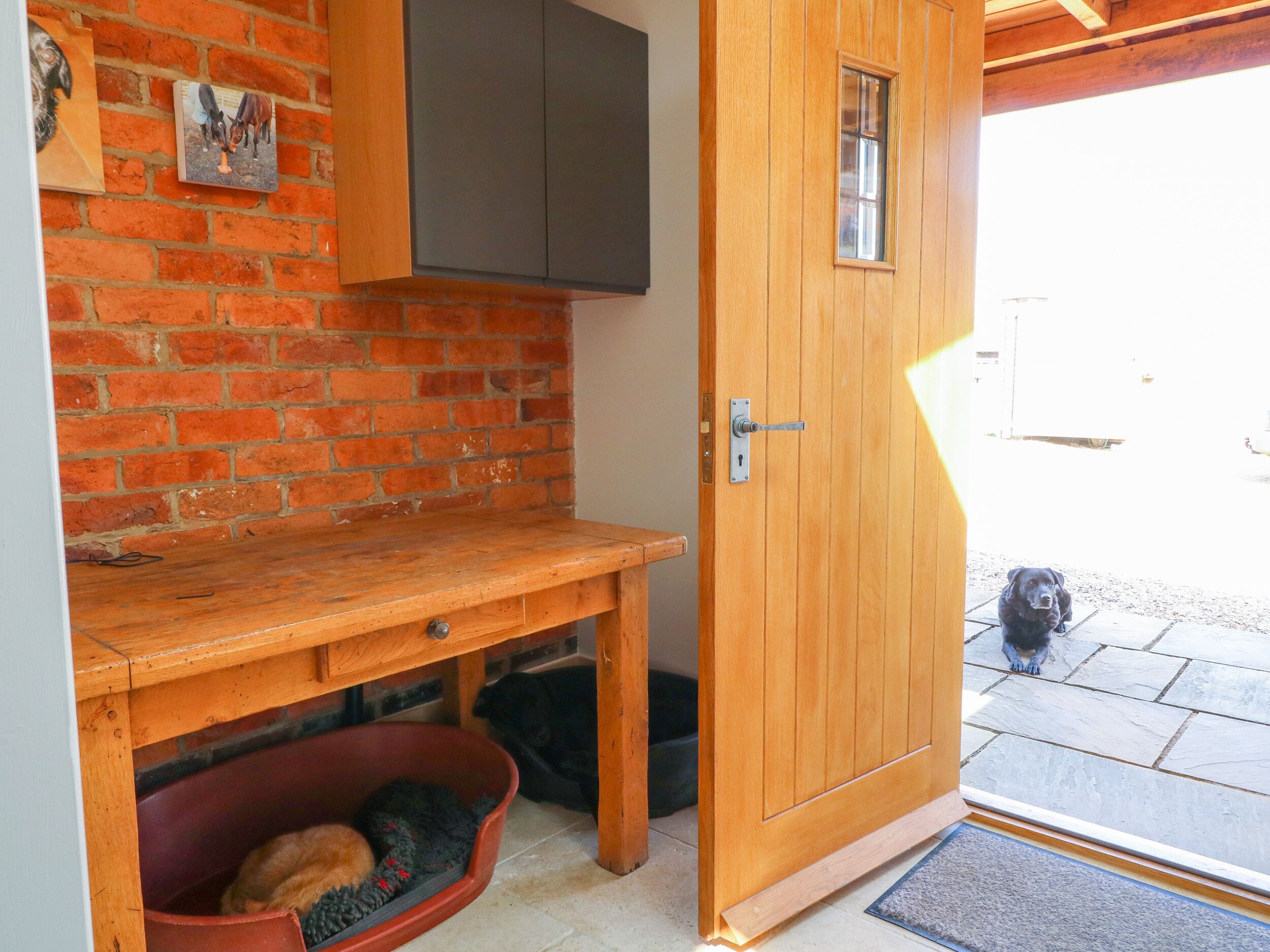 A wooden door with a small window, a brick wall, a wooden bench, and a dog bed with a dog inside.