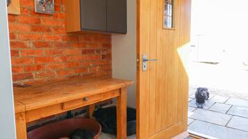A wooden door with a small window, a brick wall, a wooden bench, and a dog bed with a dog inside.