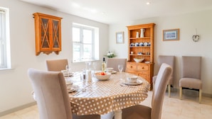 A dining area with a round table set for four, surrounded by chairs. There is a wooden cabinet with dishes and a vase on top. - Grooms Cottage (Leicester)