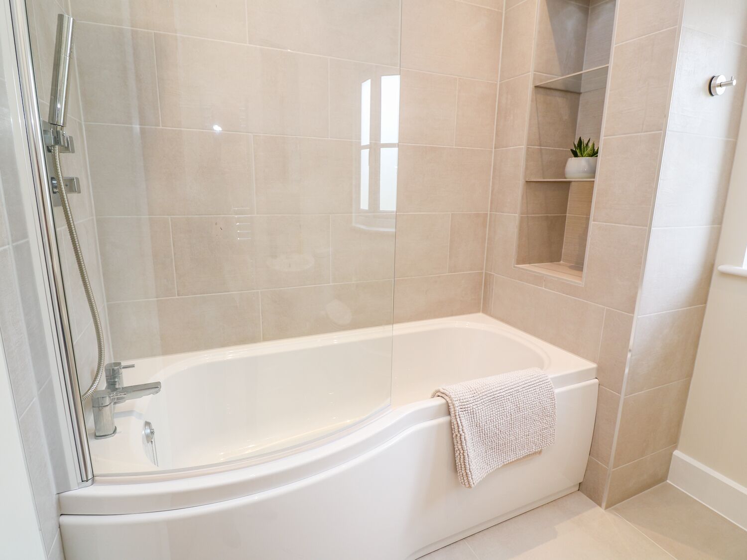 A modern bathroom with a freestanding bathtub, a glass-enclosed shower, and a small shelf with a plant.