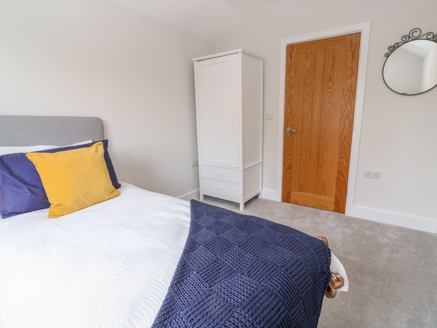 A bedroom with a bed, a wardrobe, a wooden door, and a wall-mounted mirror.