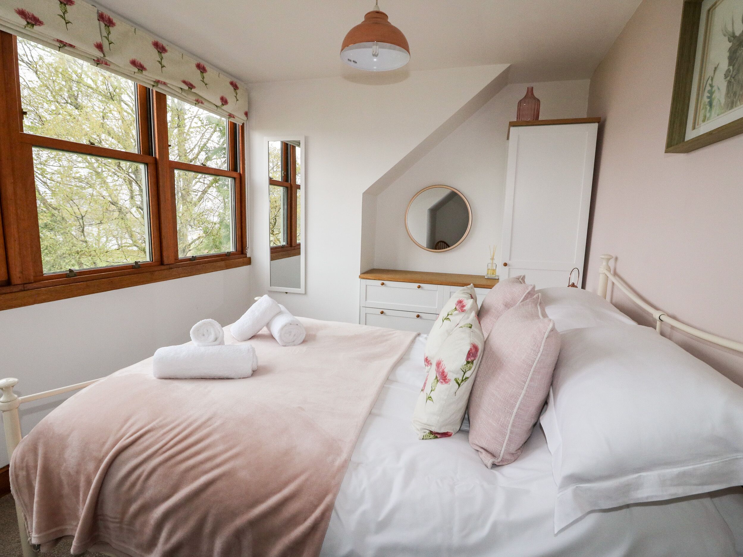 A bedroom with a bed, a dresser, a mirror, and a window with floral curtains.
