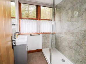 A bathroom with a shower, a sink, and a window with curtains. - Clearwater House (Lochailort)